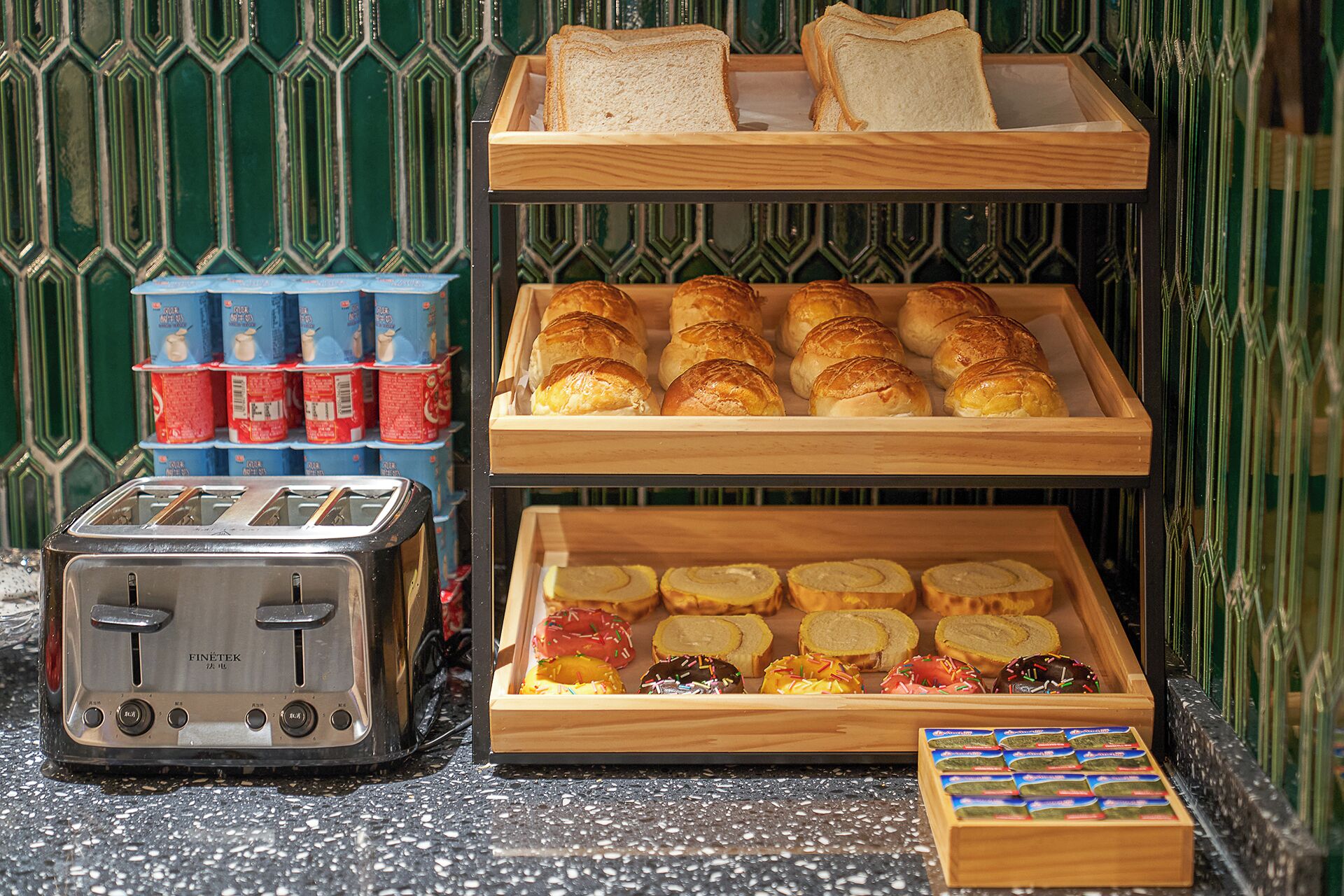 Un buffet de petit-déjeuner comprenant diverses viennoiseries et pains, un grille-pain et des boissons emballées.