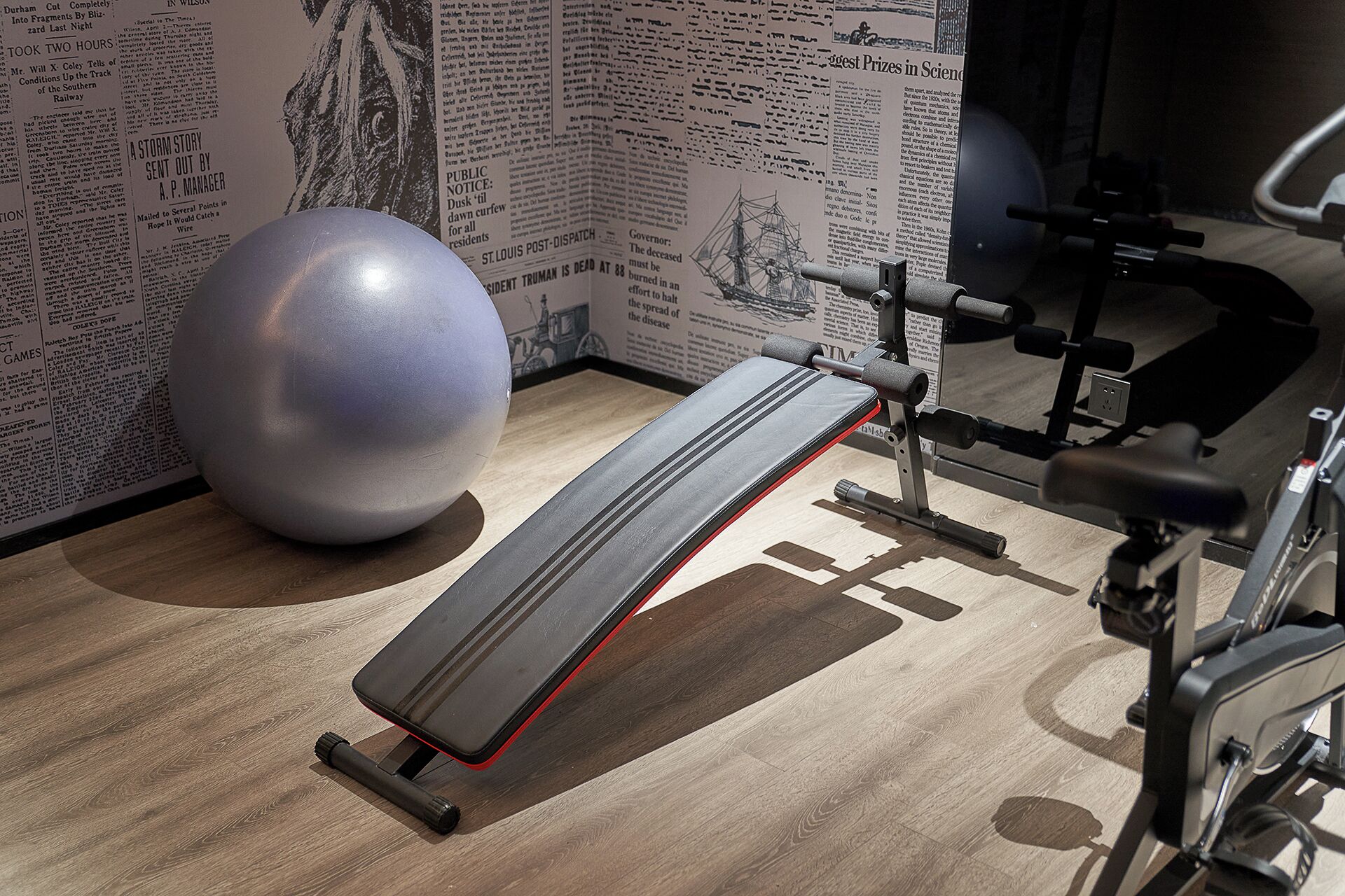 A gym with a bench, a large exercise ball, and a weight machine.