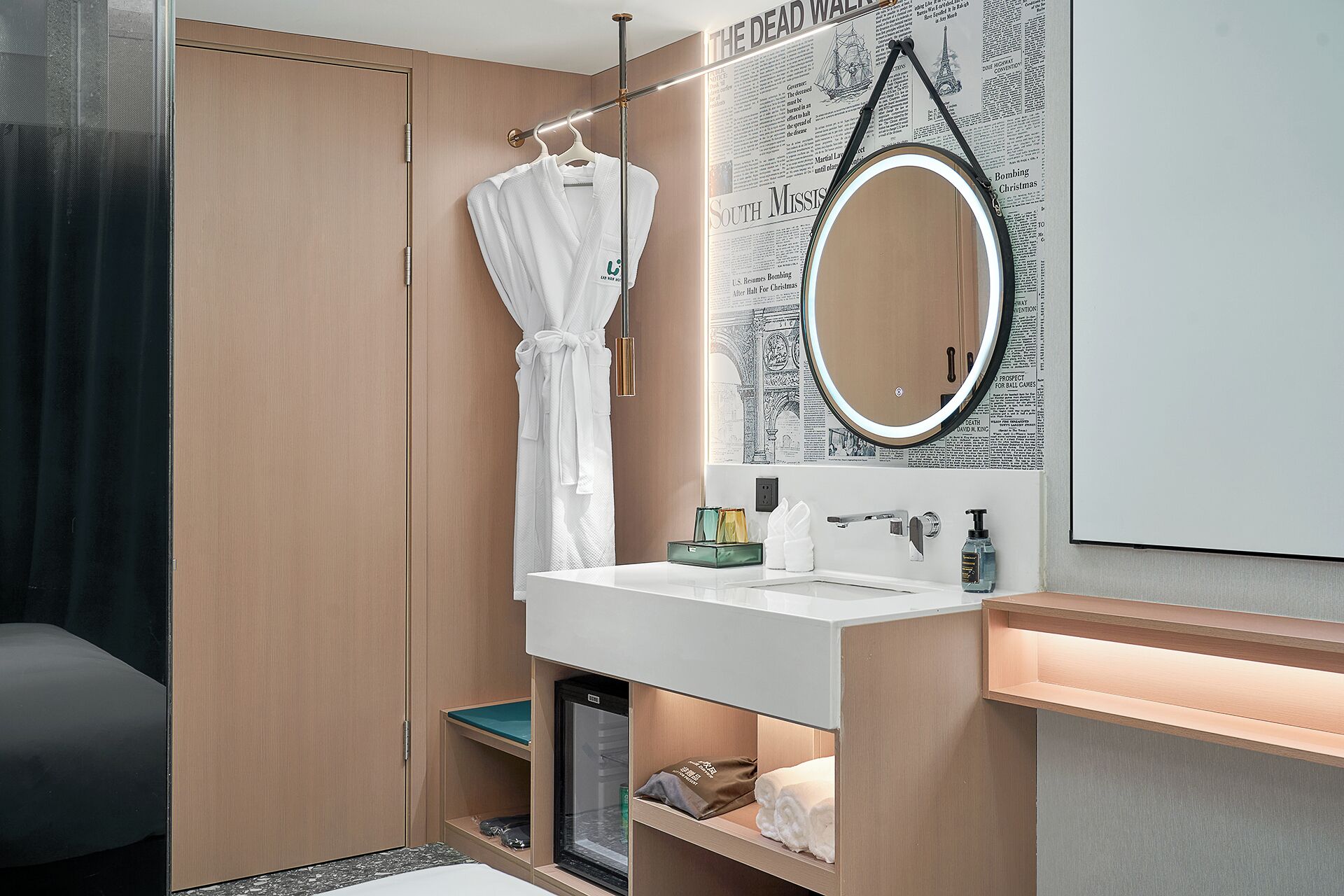 Un baño moderno con tocador de madera, un espejo redondo y una bata colgada en un perchero.