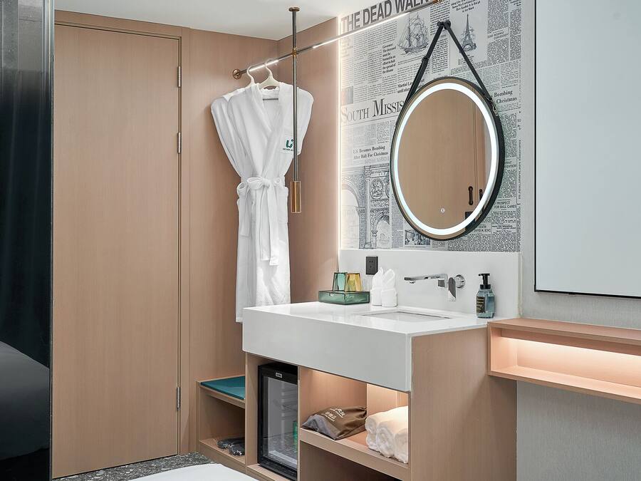 Un bagno moderno con un mobile bagno in legno, uno specchio rotondo e un accappatoio su un appendiabiti.