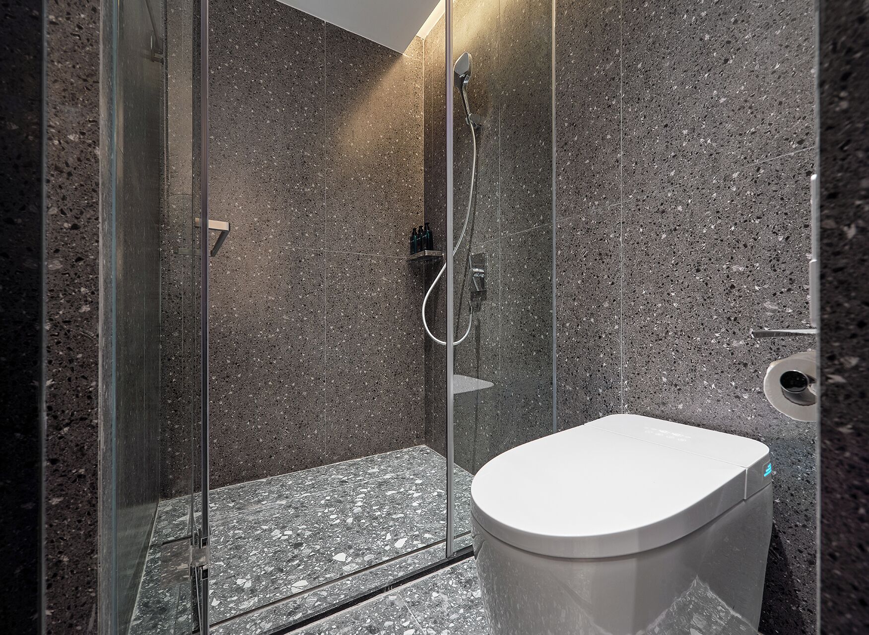A modern bathroom with a glass-enclosed shower, a white toilet, and a marble-tiled wall.
