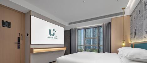 Ein Hotelzimmer mit einem Bett, einem großen Fenster, einem an der Wand befestigten Fernseher und einer Tür mit Kartenleser.