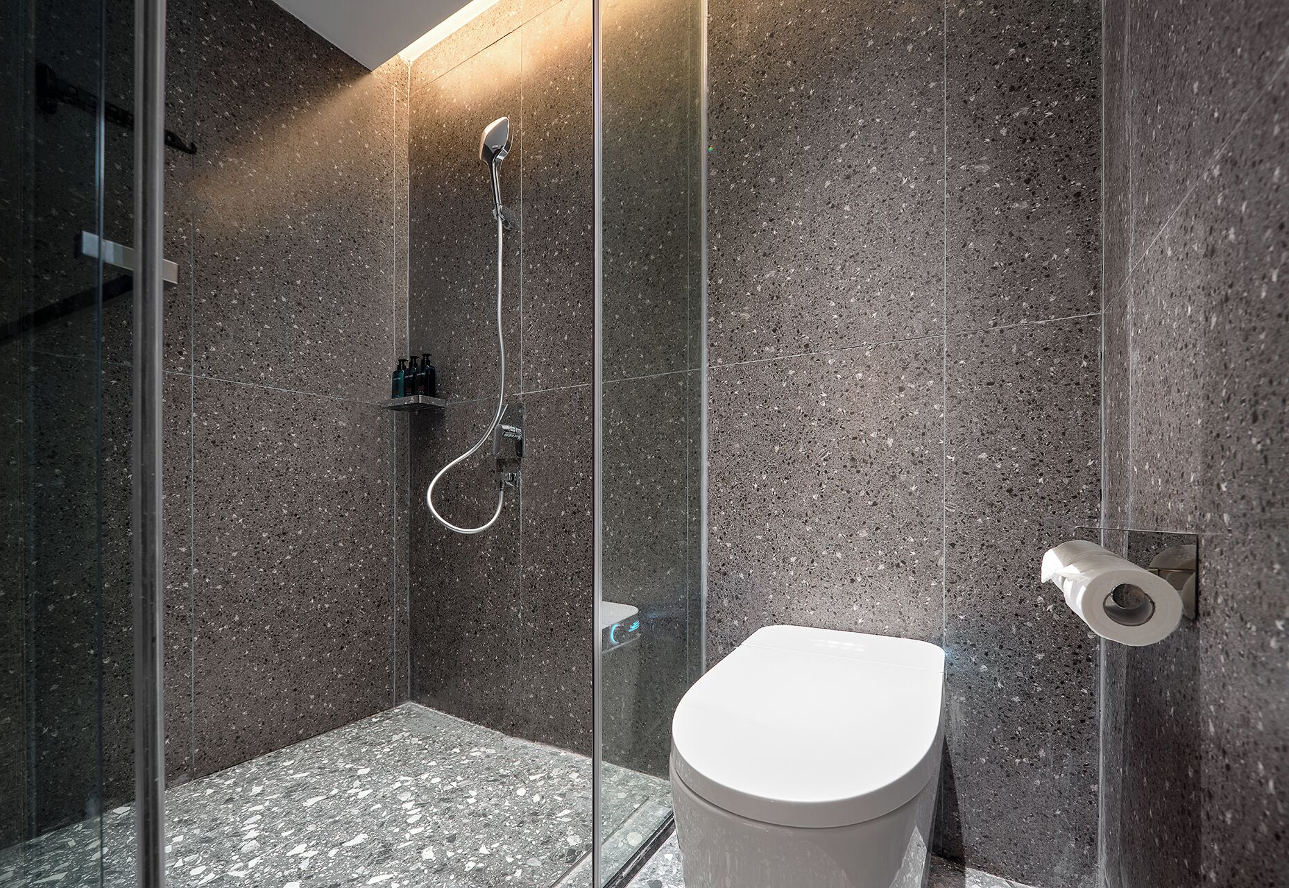 Een moderne badkamer met een douchecabine van glas, een wit toilet en een marmeren vloer.