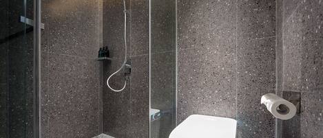 Een moderne badkamer met een douchecabine van glas, een wit toilet en een marmeren vloer.
