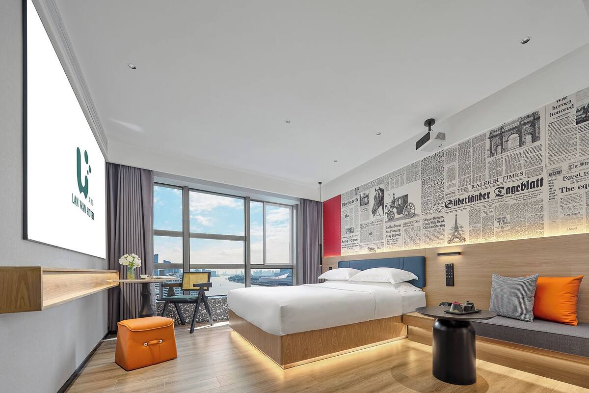 A modern hotel room with a large bed, a desk, and a seating area.