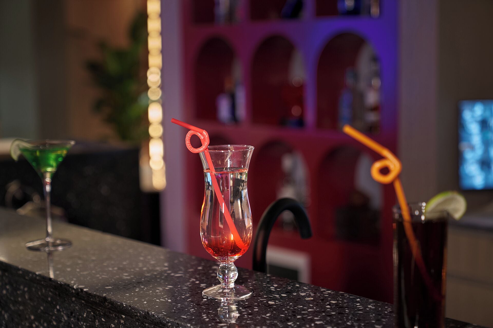 A bar area with two glasses of red cocktails, one with a red straw and the other with an orange straw.