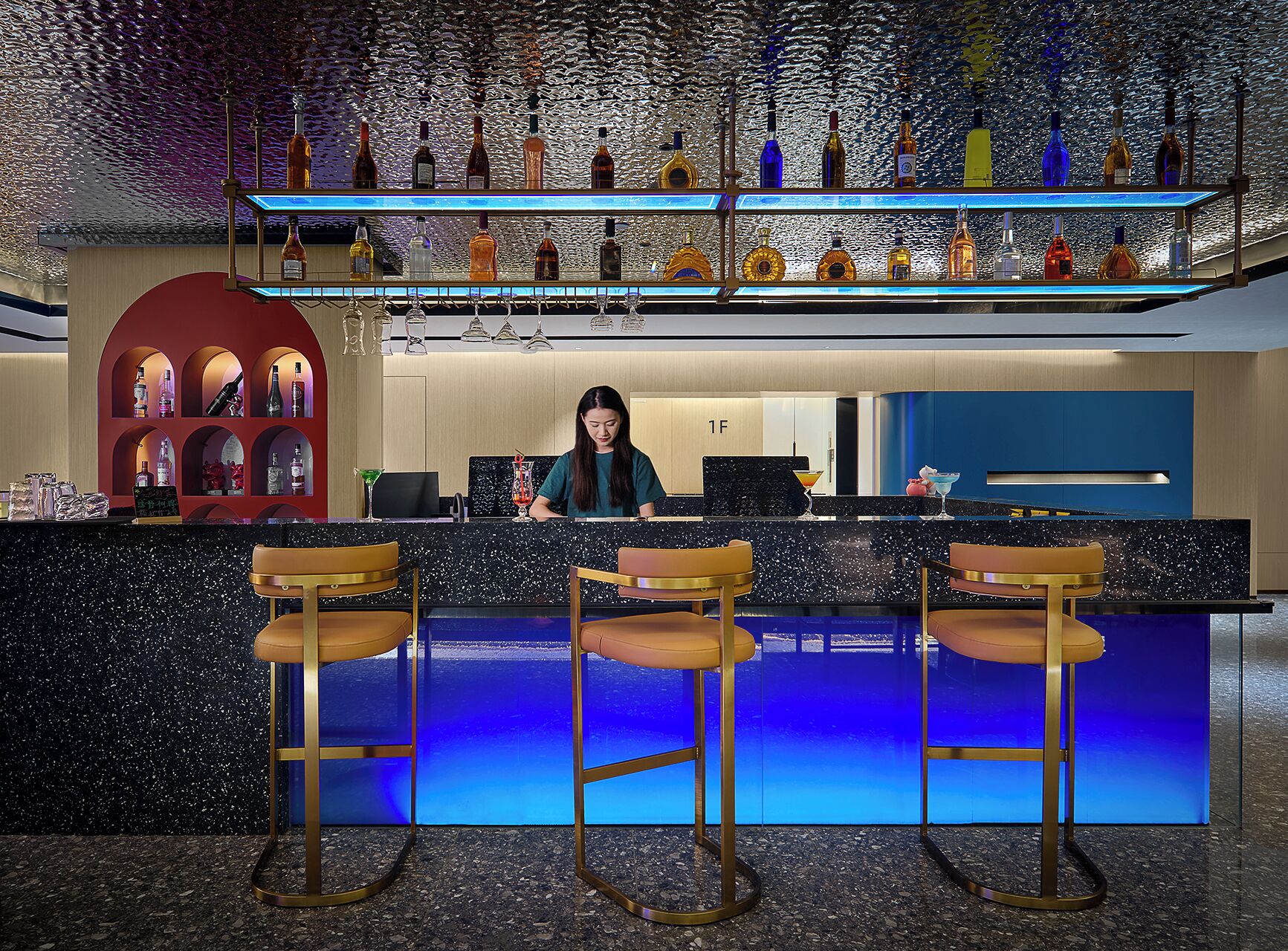 A bar area with a bartender, bar stools, and shelves of liquor bottles.