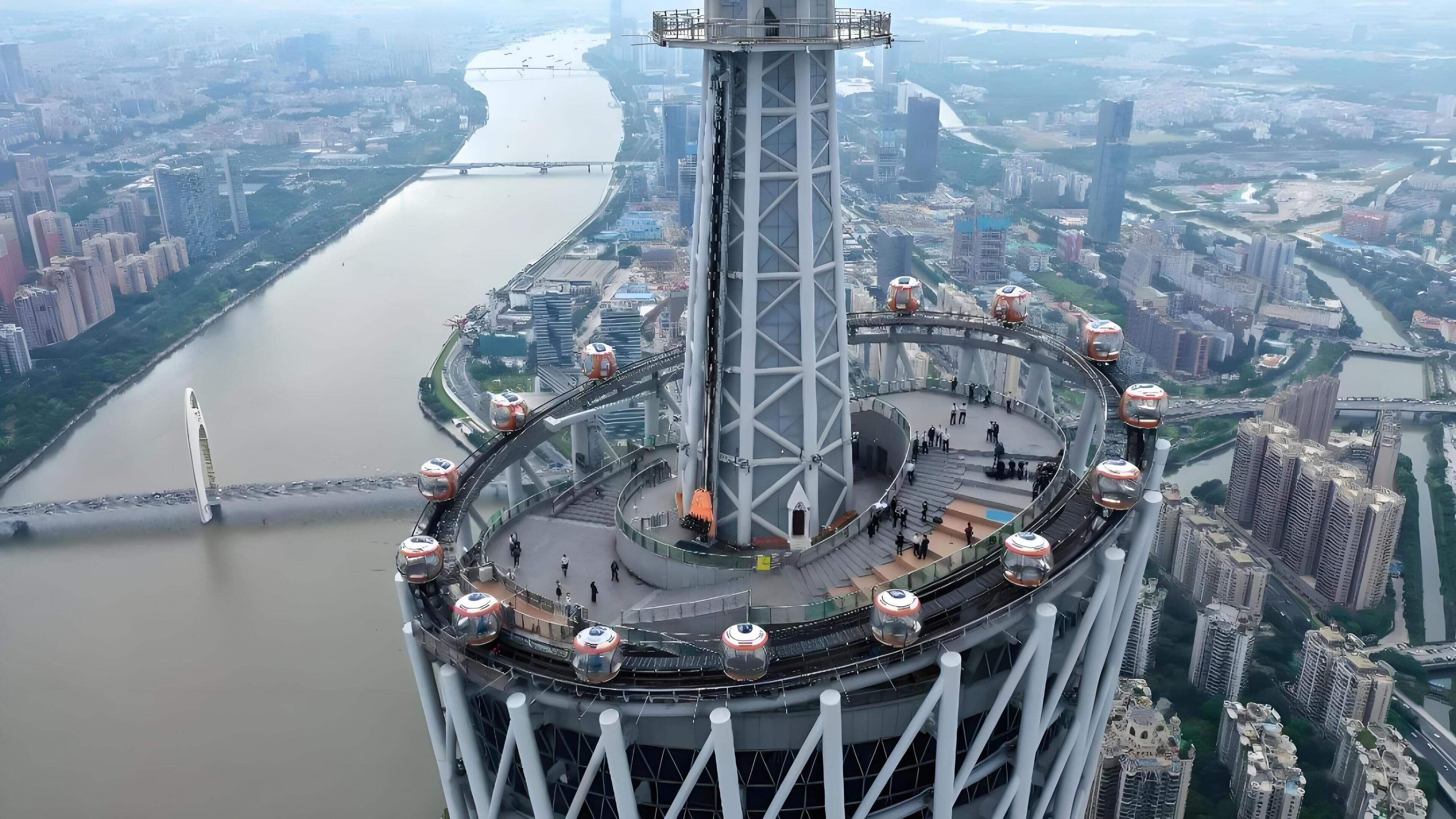 A high-rise building with a circular observation deck and a river in the background.