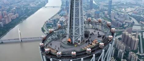 A high-rise building with a circular observation deck and a river in the background.