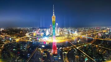 Paisagem urbana noturna com uma torre imponente iluminada em várias cores.