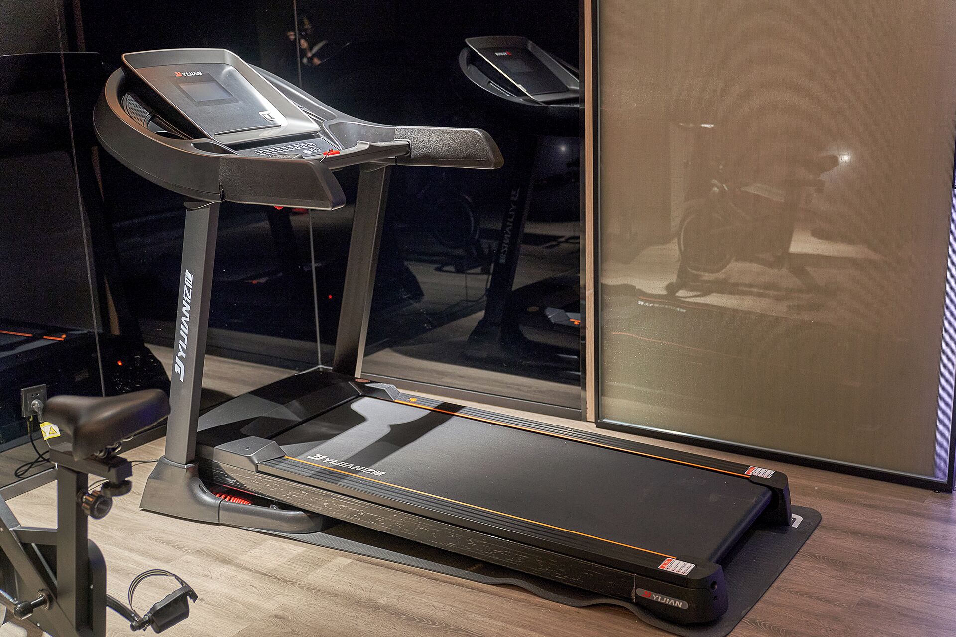 A treadmill in a room with a wooden floor and a large window.
