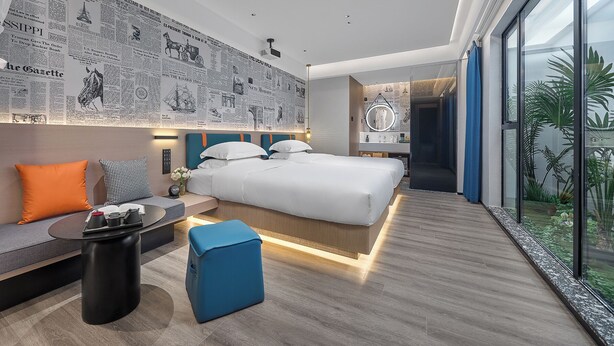 A modern hotel room with a large bed, a seating area with a coffee table, and a view of a tropical garden through large windows. - Lan Wan International Hotel  (Guangzhou)