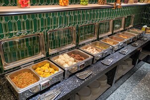 Ein Buffet mit verschiedenen Speisen in Metallbehältern, einer grün gefliesten Rückwand und einer fleckigen Arbeitsplatte.