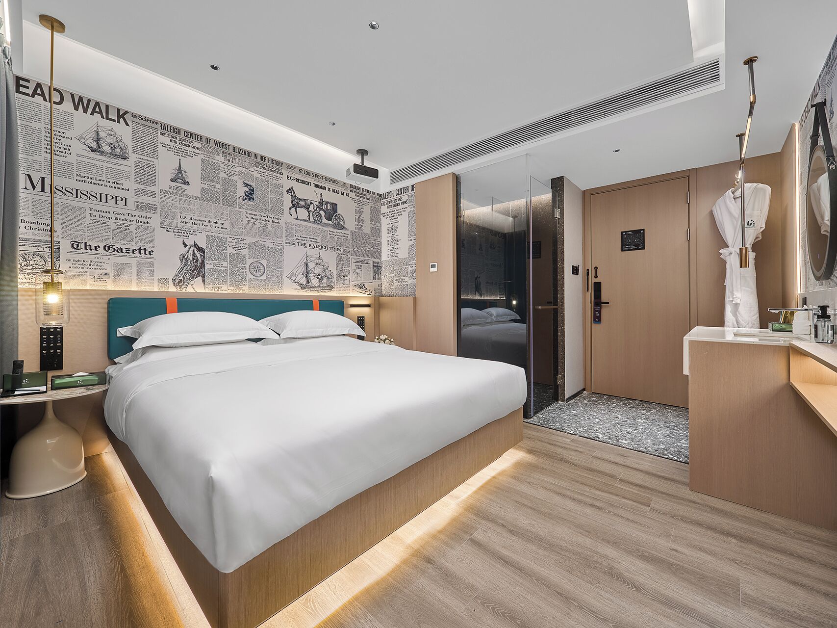 A modern hotel room with a large bed, a wooden headboard, a glass shower enclosure, and a wall decorated with newspaper clippings.