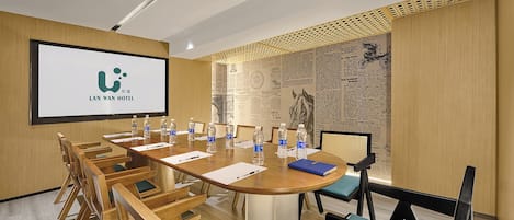 A conference room with a large screen displaying the Lan Wan Hotel logo, a long table with chairs, water bottles, and notepads.