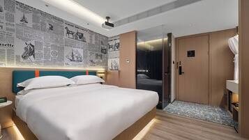 A hotel room with a large bed, a headboard with newspapers, a wooden floor, and a door leading to a bathroom.