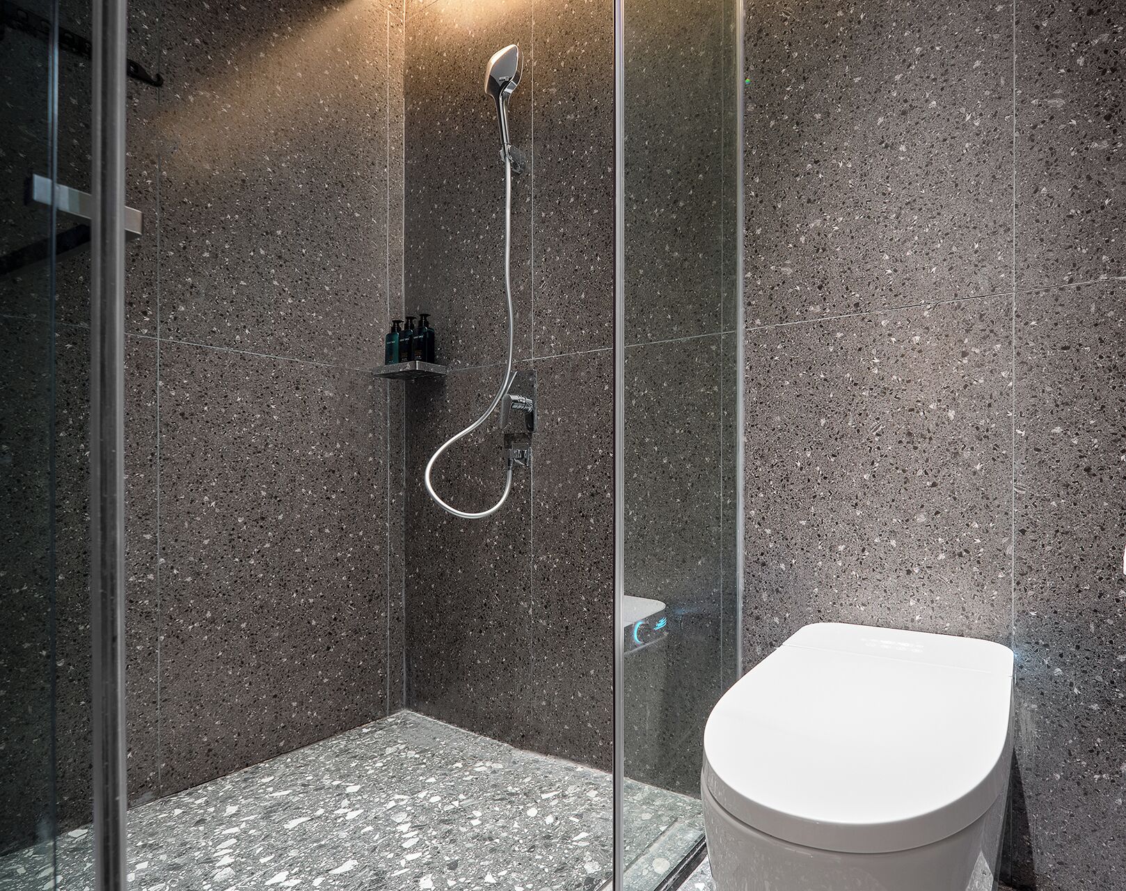 A modern bathroom with a glass-enclosed shower, a white toilet, and a granite-tiled floor.