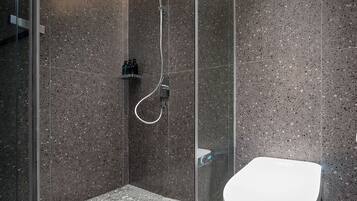 A modern bathroom with a glass-enclosed shower, a white toilet, and a granite-tiled floor.