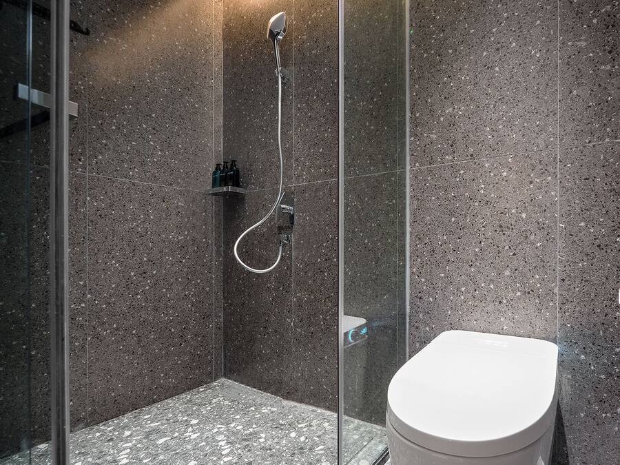 A modern bathroom with a glass-enclosed shower, a white toilet, and a granite-tiled floor.