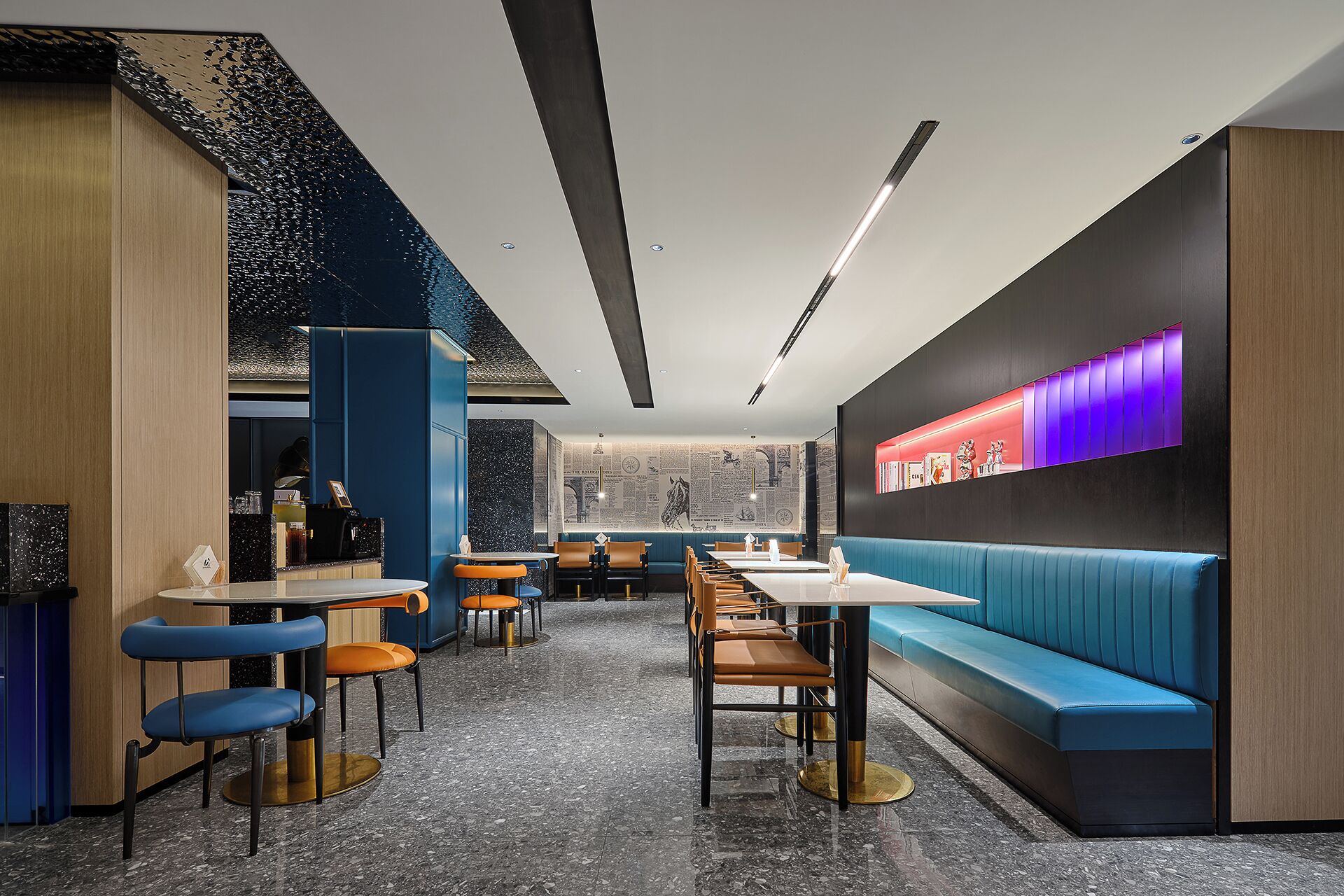 Un intérieur de restaurant moderne avec des sièges bleus et noirs, un espace bar et un mur orné d’une enseigne lumineuse.