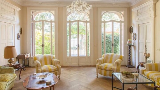 Une pièce avec deux fauteuils à rayures jaunes, une table basse en verre et un lustre.