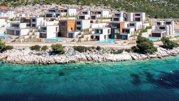 Ein Küstenresort mit modernen Villen, einer felsigen Küstenlinie und klarem, türkisblauem Wasser.