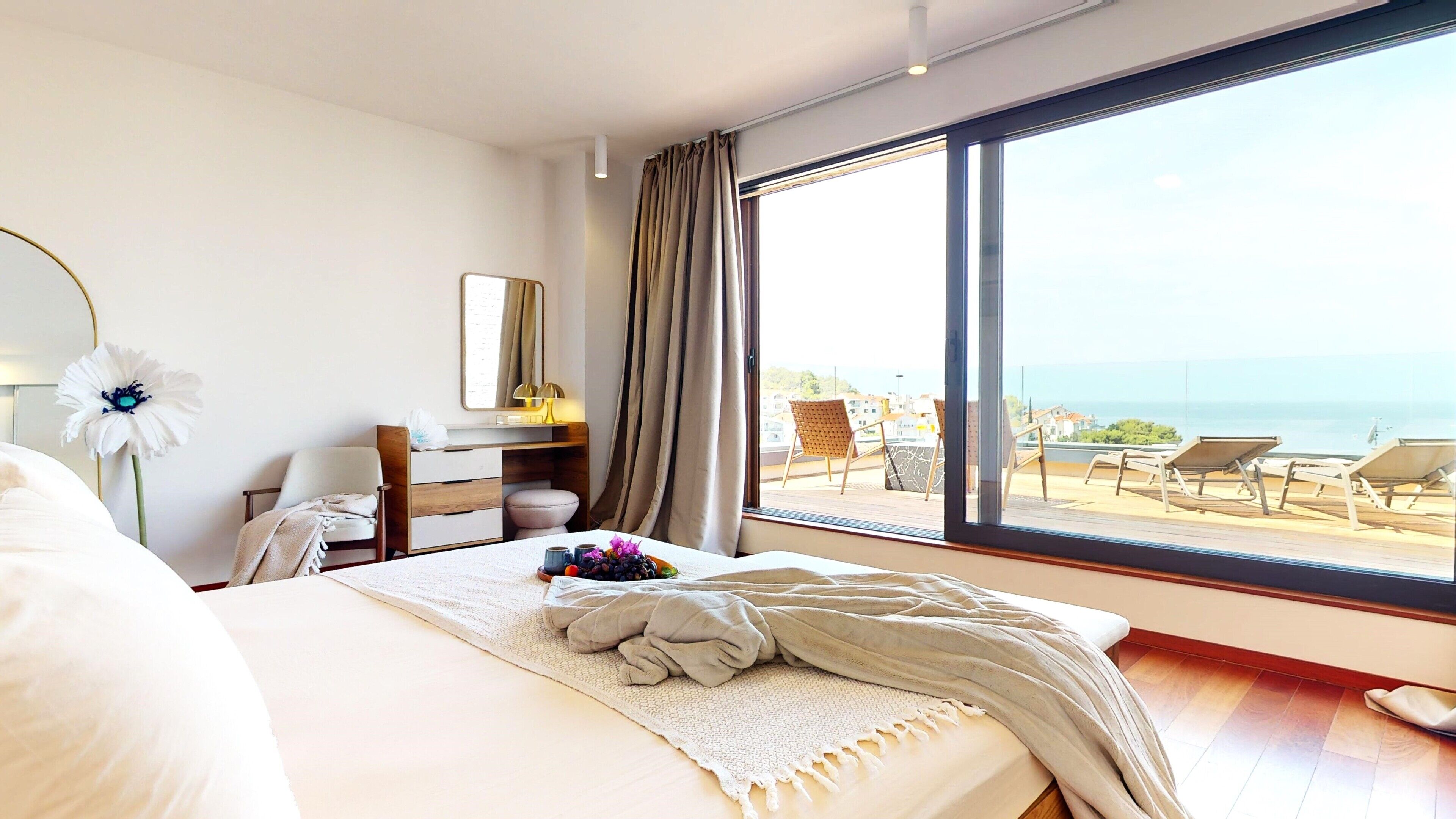 A hotel room with a large window, a bed, a desk, and a chair.