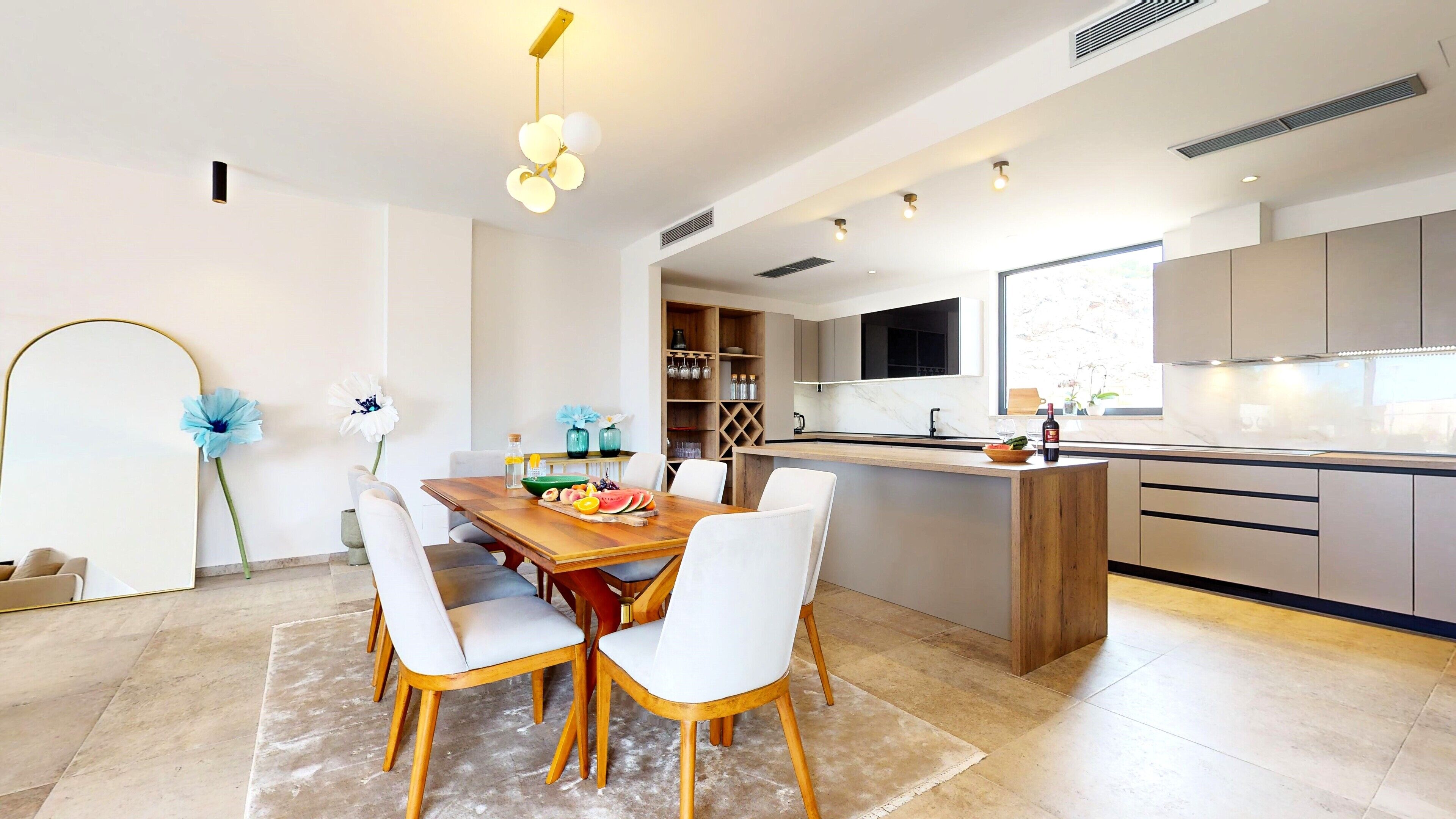 A modern kitchen with a central island, white cabinetry, and a dining area with a wooden table and chairs.