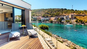 Eine moderne Villa mit einer Holzdachterrasse mit Blick auf das klare, blaue Meer, einem Pool und einer Aussicht auf die umliegende Hügelstadt.