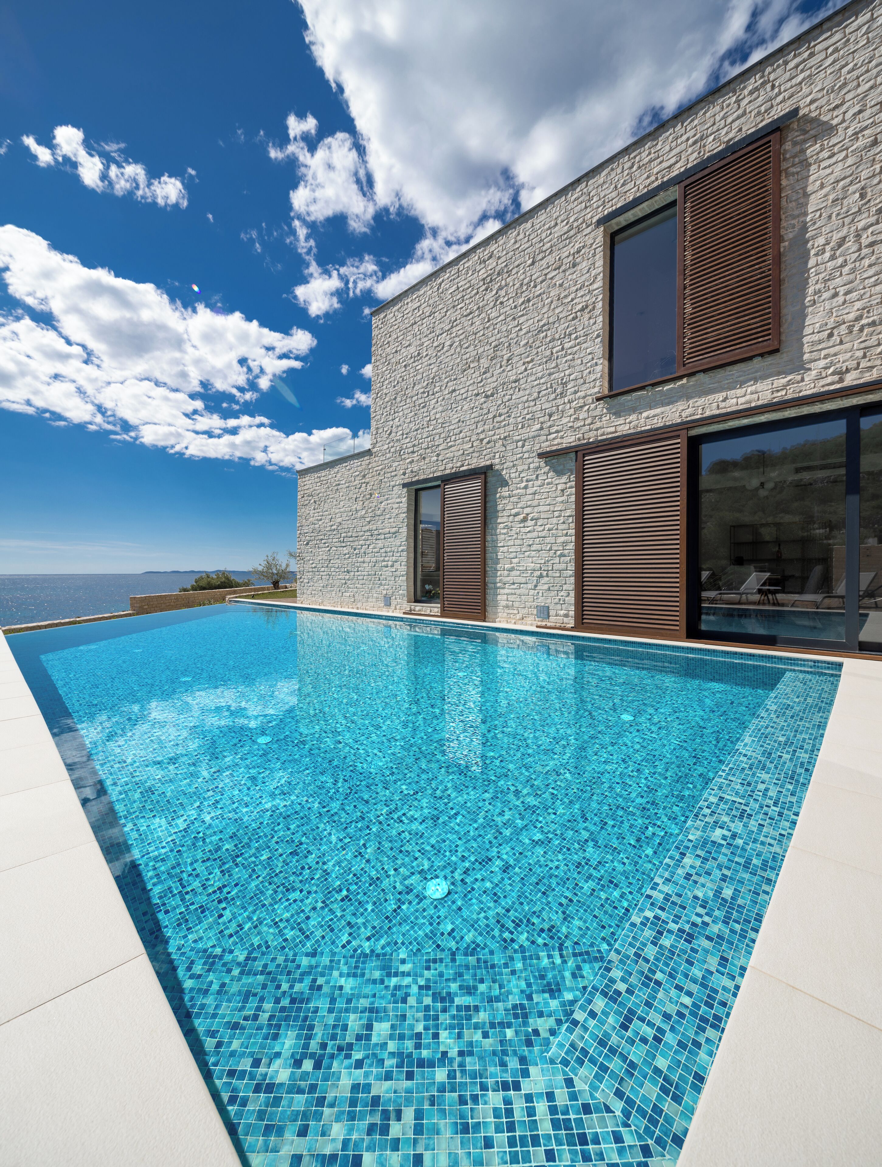 Una casa moderna con piscina, ampie finestre e vista mare.