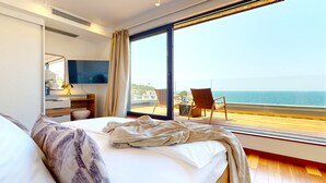 Ein Hotelzimmer mit einem großen Bett, einem Fernseher, einem Schreibtisch und Meerblick.