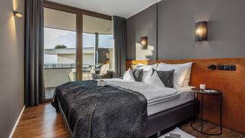 Ein modernes Hotelzimmer mit einem großen Bett, einem kleinen Nachttisch, einem Beistelltisch und Blick ins Freie.