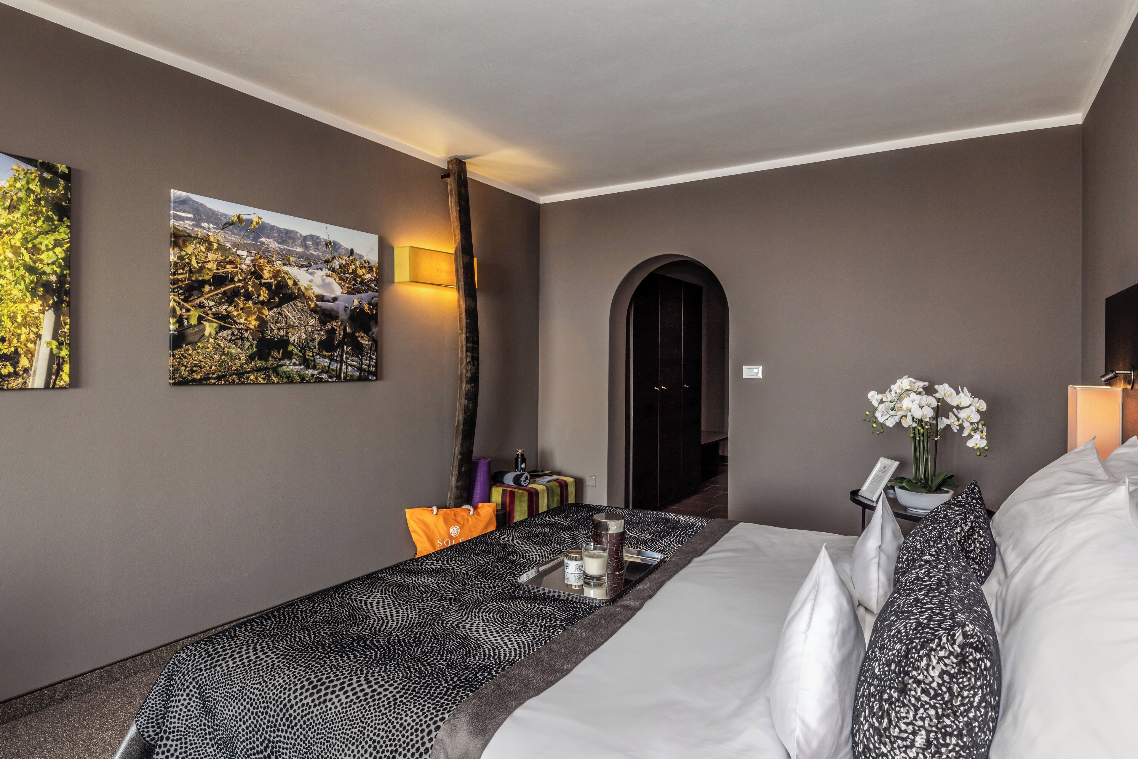 A hotel room with a bed, a nightstand, a vase with flowers, and a painting on the wall.