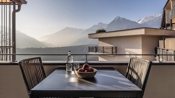 Ein Balkon mit Tisch, Stühlen, einer Obstschale und einer Flasche.