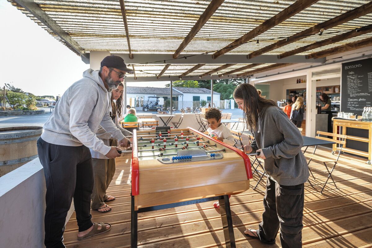 Une table de baby-foot en bois, placée sous un toit métallique, avec en arrière-plan la vue d’un immeuble.