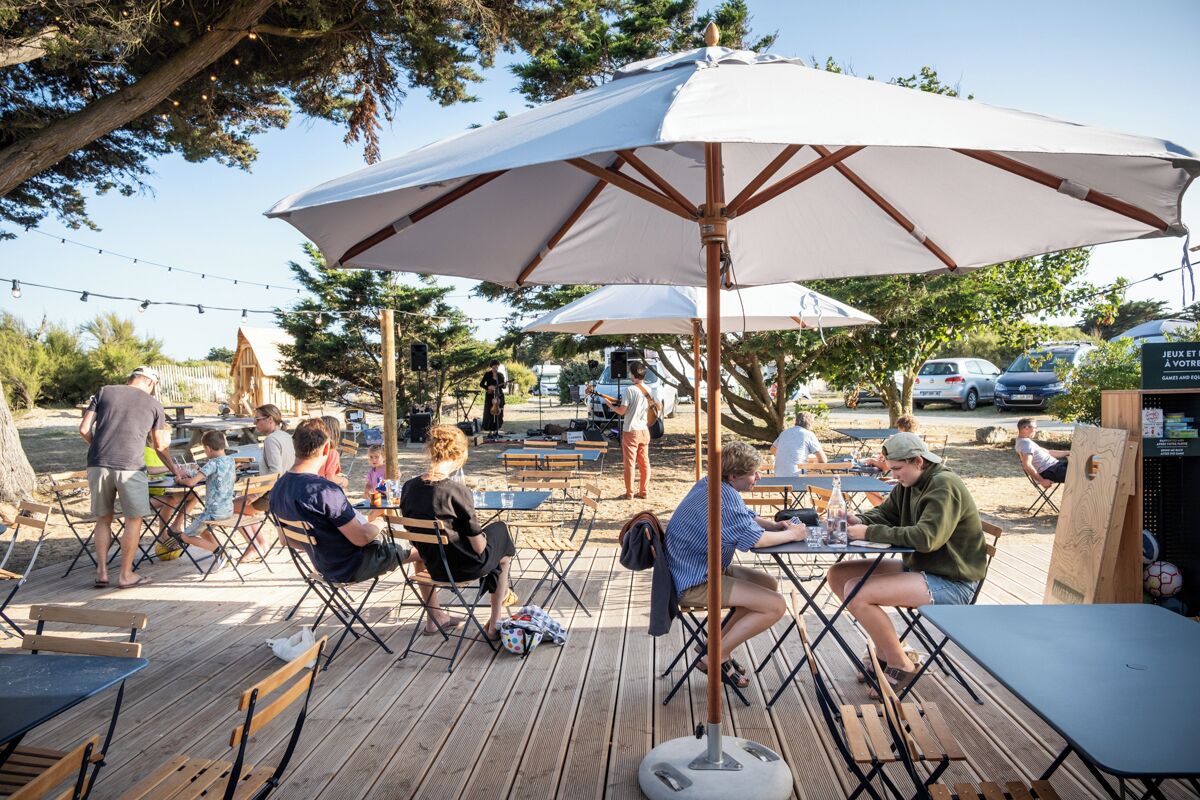 An outdoor dining area with wooden tables and chairs, umbrellas, and string lights.