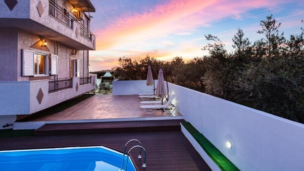 A rooftop with a swimming pool, lounge chairs, and a view of the sunset.