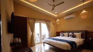 Une chambre à coucher comprenant un lit, un ventilateur de plafond, un climatiseur, une table de chevet et une fenêtre avec des rideaux.