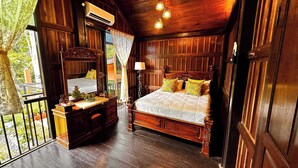 Quarto de madeira com cama, mesa de cabeceira, luminária e vista para o verde lá fora.