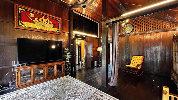 Interior em madeira com televisão, tapete estampado, uma cadeira e um objeto decorativo na parede.