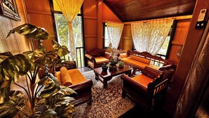 Interior em madeira com sofá, mesa de centro e grandes vasos de plantas.