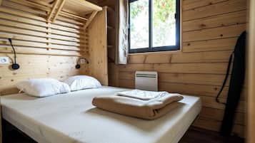 Une pièce de cabane en bois comprenant un lit, une fenêtre donnant sur la forêt et un radiateur.