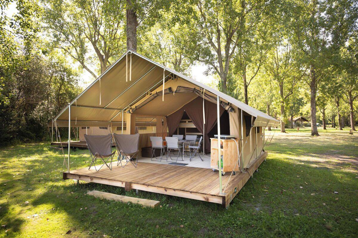 A tented accommodation with a wooden deck, foldable chairs, and a table set up for dining.