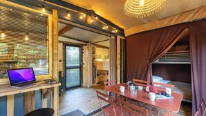 A cozy room with a wooden desk, a laptop, a table with chairs, a bed, and a hanging light fixture.