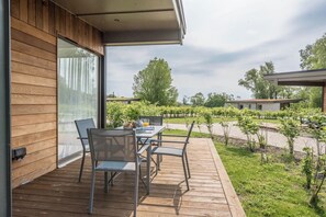 A wooden deck with a table and chairs, overlooking a vineyard and a grassy area with trees.
