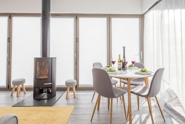 A modern dining area with a central table, chairs, and a wood-burning stove.