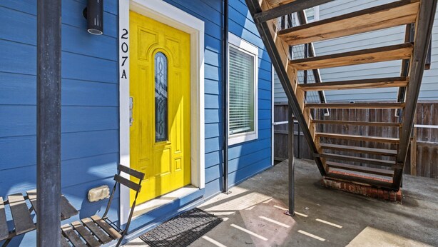 A blue house with a yellow door, a wooden bench, and a wooden staircase.