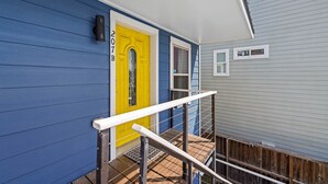 Een meerlaags huis met een gele deur, blauwe bekleding en een witte balustrade op het bovenste niveau.