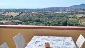 Ein Balkon mit Tisch und Stühlen mit Blick auf eine Küstenlandschaft mit Grünflächen und Gebäuden.