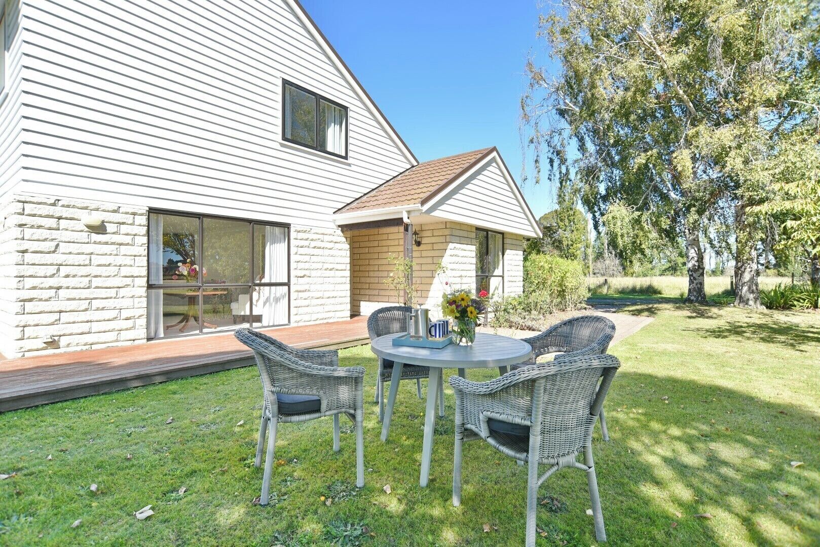 A house with a large window and a patio with wicker chairs and a table.